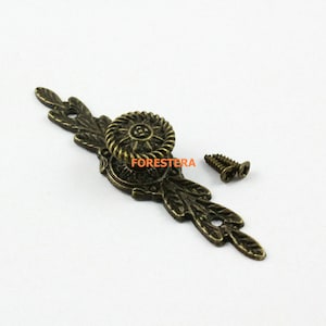 May include: Antique brass drawer pull with a floral design and a round knob. The pull is attached to a surface with two screws.