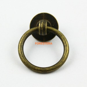 May include: Antique brass ring pull cabinet door handle with a round base. The handle is a single ring with a smooth finish.