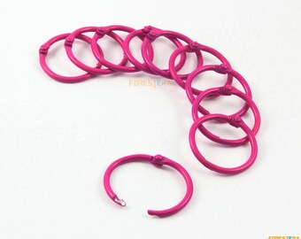 Può includere: Un set di dieci anelli di rilegatura in metallo rosa. Gli anelli sono aperti e pronti per essere utilizzati per rilegare carte o altri materiali.