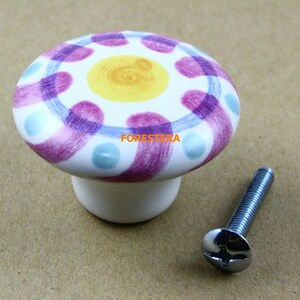 May include: A white ceramic knob with a purple, blue, and yellow swirl design. The knob comes with a silver screw.