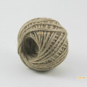 Puede incluir: Una bola de cuerda natural hecha de fibra de yute. La cuerda es de color marrón claro y está enrollada en forma de bola.