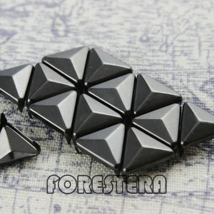 May include: A close-up of a group of black triangular pyramid-shaped metal studs. The studs are arranged in a pattern and have a shiny finish.