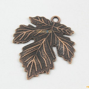 May include: A copper-colored metal leaf charm with a detailed design and a loop for hanging. The leaf has a textured surface and a slightly aged appearance.