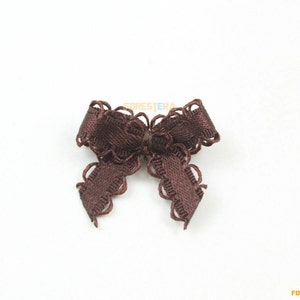 May include: A small, dark brown satin bow with a scalloped edge. The bow is centered and appears to be made of a ribbon material. The bow is a decorative element, likely for crafts or embellishments.