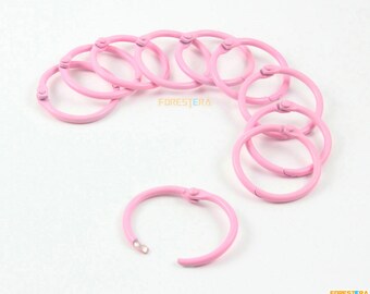 Può includere: Dieci anelli di rilegatura in metallo rosa, ognuno con un diametro di circa 2,5 cm. Gli anelli sono aperti e pronti per essere utilizzati per rilegare documenti.