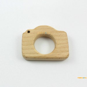May include: A wooden camera-shaped teether for babies. The teether is made of natural wood and has a smooth, rounded surface.
