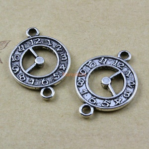 Puede incluir: Dos dijes de cara de reloj plateados con diseños de círculo abierto y los números del 1 al 12. Cada dije tiene dos anillos de salto para sujetar a las joyas.