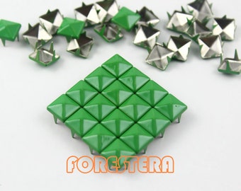 Puede incluir: Un grupo de 36 tachuelas de metal de forma piramidal verde con bases plateadas. Las tachuelas están dispuestas en un patrón cuadrado. Las tachuelas se utilizan para manualidades y decoración.