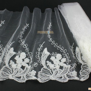 May include: White embroidered lace trim with a floral design. The lace is delicate and has a soft, flowing texture.