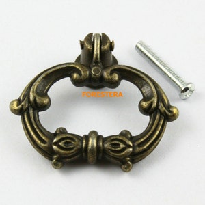 May include: Antique bronze cabinet pull with an ornate design and a single screw. The pull has a ring shape with a decorative bow in the center.