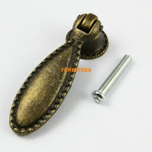 May include: Antique gold-toned cabinet pull with an oval-shaped handle and a decorative border. The pull comes with a silver screw.