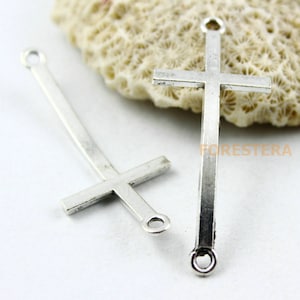 May include: Two silver-toned metal cross charms with a loop at the top for attaching to jewelry or other crafts. The crosses are simple and elegant, with a slightly textured finish.