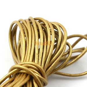 Puede incluir: Primer plano de un carrete de cordón de cuero dorado. El cordón es suave y flexible, y es perfecto para hacer joyas, accesorios y otros proyectos.