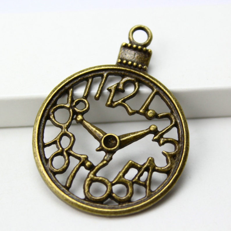 May include: Antique gold-toned metal clock charm with Roman numeral markings and openwork design. The charm has a loop at the top for attaching to jewelry or crafts.