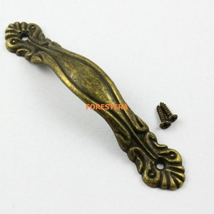 May include: Antique brass cabinet pull with ornate details and a curved shape. The pull comes with two screws for installation.