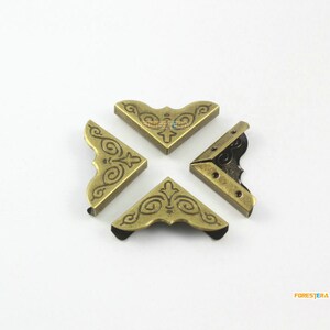 May include: Four gold-toned metal corner protectors with a decorative, ornate design. The corner protectors are arranged in a cross shape.