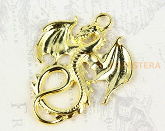 May include: Gold-toned metal dragon charm with wings outstretched and a curled tail. The dragon is detailed with scales and has a loop at the top for hanging.