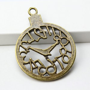May include: A bronze-colored metal charm shaped like a clock face with Roman numerals and a cutout design. The charm has a loop at the top for attaching to a necklace or bracelet.