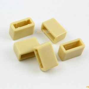 May include: Five beige plastic rectangular belt loops. The loops are hollow with a rectangular opening. The word "FORESTERA" is printed on the right side of the image.