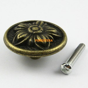 Puede incluir: Un pomo de armario redondo de color dorado antiguo con un diseño floral. El pomo viene con un tornillo plateado.