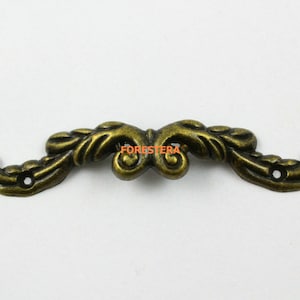 May include: Antique gold-toned metal decorative hardware with a floral design. The hardware has two holes for attaching to a surface.