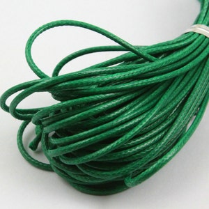 May include: A spool of green waxed cotton cord. The cord is tightly wound and has a smooth, polished finish.