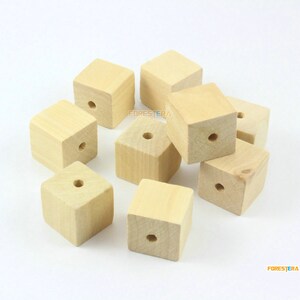 Peut inclure: Dix cubes en bois non finis avec un trou percé au centre de chaque cube. Les cubes sont disposés en pile sur une surface blanche.