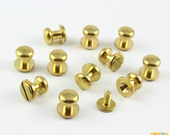 Könnte beinhalten: Eine Sammlung von 10 goldfarbenen Metallknöpfen mit Schraubdesign. Die Knöpfe haben eine runde, gewölbte Oberseite und eine flache Unterseite. Die Knöpfe sind in einem zufälligen Muster auf einer weißen Oberfläche angeordnet.