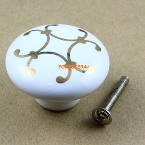 Peut inclure: Bouton de porte en céramique blanche avec un motif floral doré et une vis argentée.