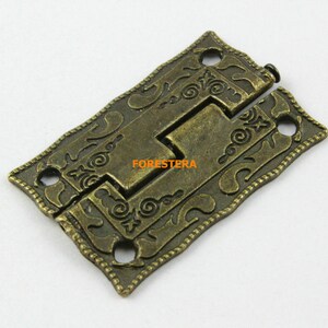 May include: Antique brass-coloured metal hinge with a decorative floral design. The hinge is rectangular and has two holes on each side.