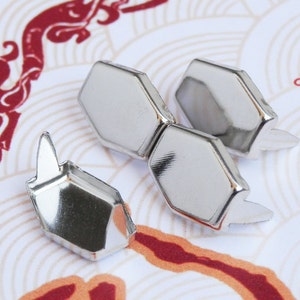 May include: Four silver metal hexagonal-shaped rivets with pointed prongs. The rivets are on a white and red patterned surface.