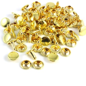 May include: A large pile of gold-colored metal rivets. The rivets have a round head and a post that is designed to be hammered into a hole.
