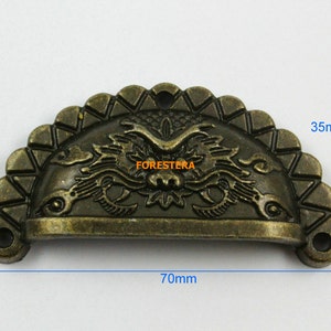 Op de afbeelding: Een halfronde, antieke messing ladegreep met een decoratief drakenontwerp. De greep is 70 mm breed en 35 mm hoog.