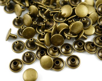 May include: A large pile of antique gold metal rivets. The rivets have a round head and a post with a hole in the center. The rivets are scattered on a white surface.