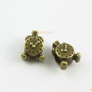 Könnte beinhalten: Zwei antike goldfarbene Metall-Uhrenanhänger mit einem detaillierten Zifferblatt und Zeigern. Die Anhänger sind für die Verwendung an einem Armband oder einer Halskette gedacht.