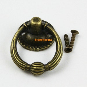 May include: Antique brass ring pull cabinet door handle with decorative details and two screws.