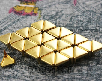 Puede incluir: Un grupo de 25 tachuelas metálicas triangulares de color dorado. Las tachuelas están dispuestas en un patrón hexagonal y tienen una punta puntiaguda. Las tachuelas se utilizan comúnmente para fines decorativos en ropa, bolsos y otros accesorios.