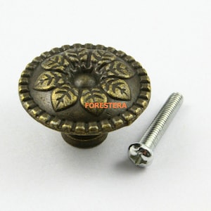 May include: A round, antique gold cabinet knob with a floral design and a matching screw. The knob has a raised, textured design of leaves and a flower in the center.