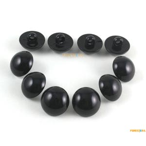 May include: A collection of black buttons and oval-shaped beads arranged on a white surface. The buttons have a loop on the back, and the beads are smooth and glossy. The word "FORESTERA" is printed on the image.