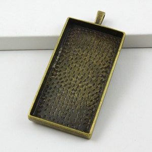 Puede incluir: Un bandeja rectangular de metal para colgante con una superficie texturizada y un bucle en la parte superior para colgar. La bandeja es de color bronce antiguo.
