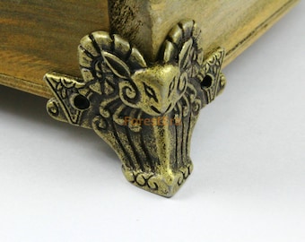 May include: A gold-toned metal furniture leg with an ornate design featuring a ram's head. The leg has a detailed, intricate design with a scroll-like pattern.