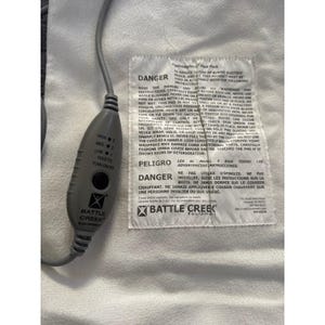 May include: A white electric heating pad with a grey handheld controller featuring a black power button and three heat settings labelled high, medium, and low. A white fabric label is sewn onto the pad with black text detailing safety warnings.