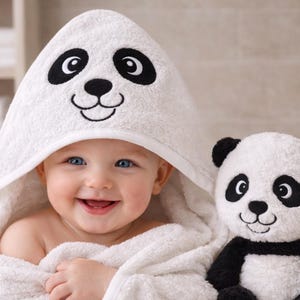Può includere: Un bambino sorridente avvolto in un asciugamano con cappuccio bianco con un design a forma di panda. Il bambino tiene in mano un peluche a forma di panda. L'asciugamano e il giocattolo sono bianchi con dettagli neri.