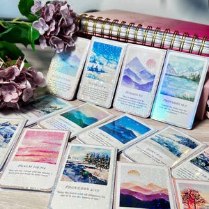 May include: A collection of rectangular cards with landscape art and Bible verses. The cards feature images of mountains, lakes, and skies, with glitter accents. The text includes verses from Psalms, Proverbs, and other books of the Bible.