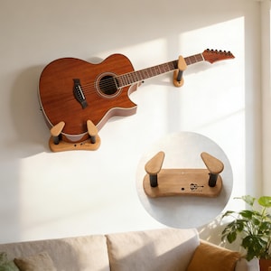 以下が含まれることがあります： 壁に取り付けられた木製のギターホルダーに展示されたアコースティックギター。ギターは茶色で、サウンドホールと指板は黒です。ホルダーは、黒いサポートが付いた明るい色の木材で作られています。