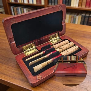 May include: Open wooden case with brass hinges, containing reeds and cork pieces. The case is lined with black fabric. A smaller, closed case with the word "abac" is visible.