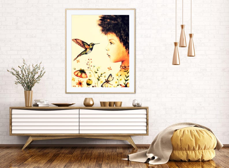 May include: A framed watercolour print showing a woman's profile and a hummingbird. The artwork includes colourful flowers and butterflies. The print is displayed above a wooden cabinet with decorative items.