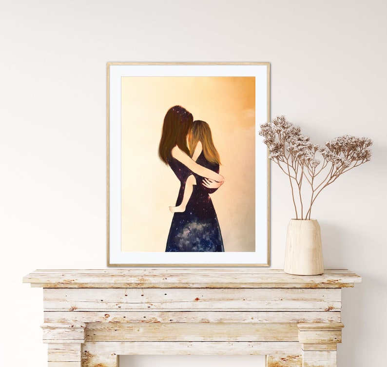 May include: A framed print of a painting depicting a woman holding a child. The woman and child are wearing dark blue dresses with a galaxy print. The background is a soft yellow.