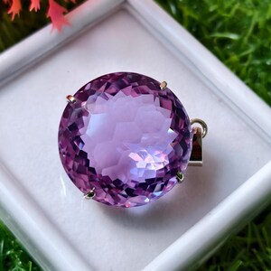 K&ouml;nnte beinhalten: Ein runder, facettierter violetter Amethyst-Anh&auml;nger in einer silberfarbenen Metallfassung mit Krappen. Der Edelstein hat einen Rundschliff mit zahlreichen reflektierenden Facetten, die f&uuml;r ein lichtfangendes Aussehen sorgen. Eine kleine &Ouml;se ist angebracht.