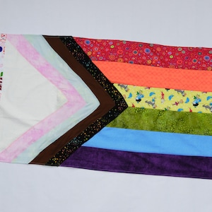 Puede incluir: Una bandera del orgullo hecha a mano con un triángulo blanco y franjas horizontales rosas, marrones, naranjas, verdes, azules y moradas. La bandera está hecha de tela y tiene un borde decorativo con la palabra "LOVE".